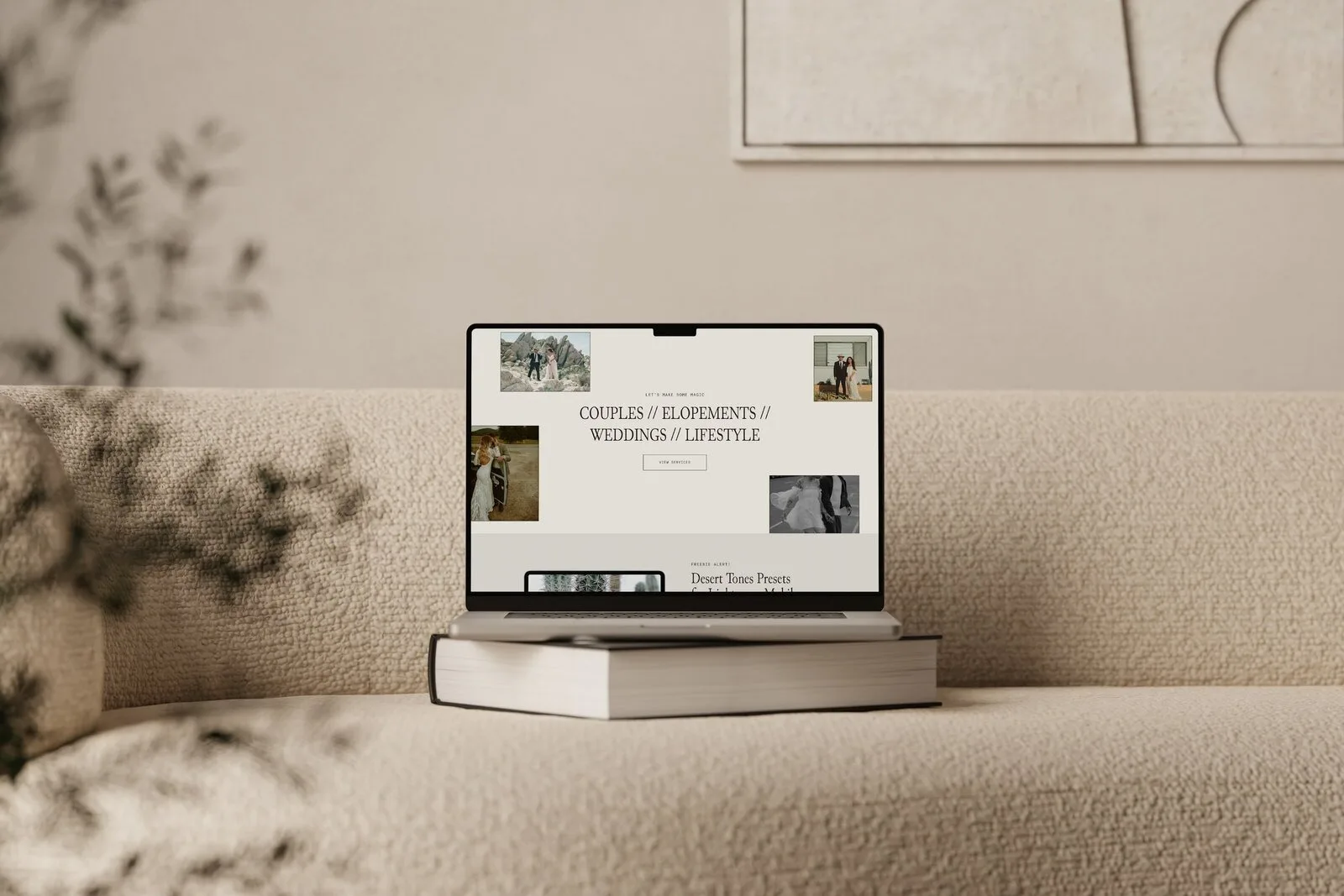 Laptop displaying a website layout on a beige sofa beside stacked books.