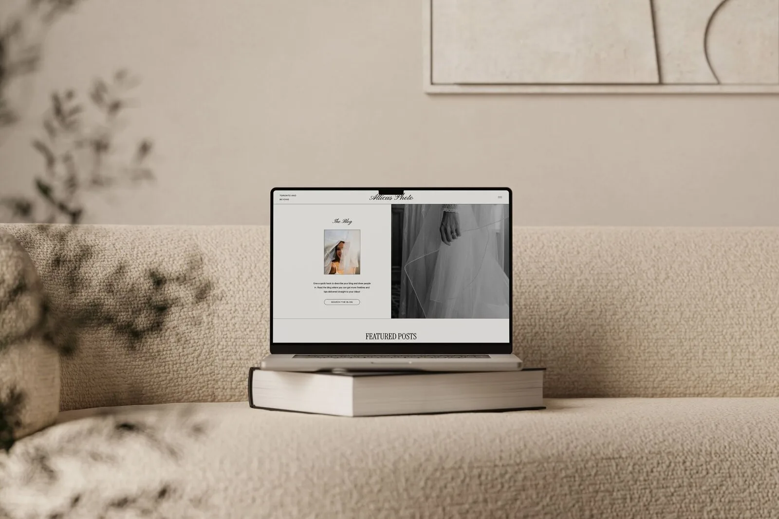 Laptop displaying a website mockup on stacked books beside a beige sofa.