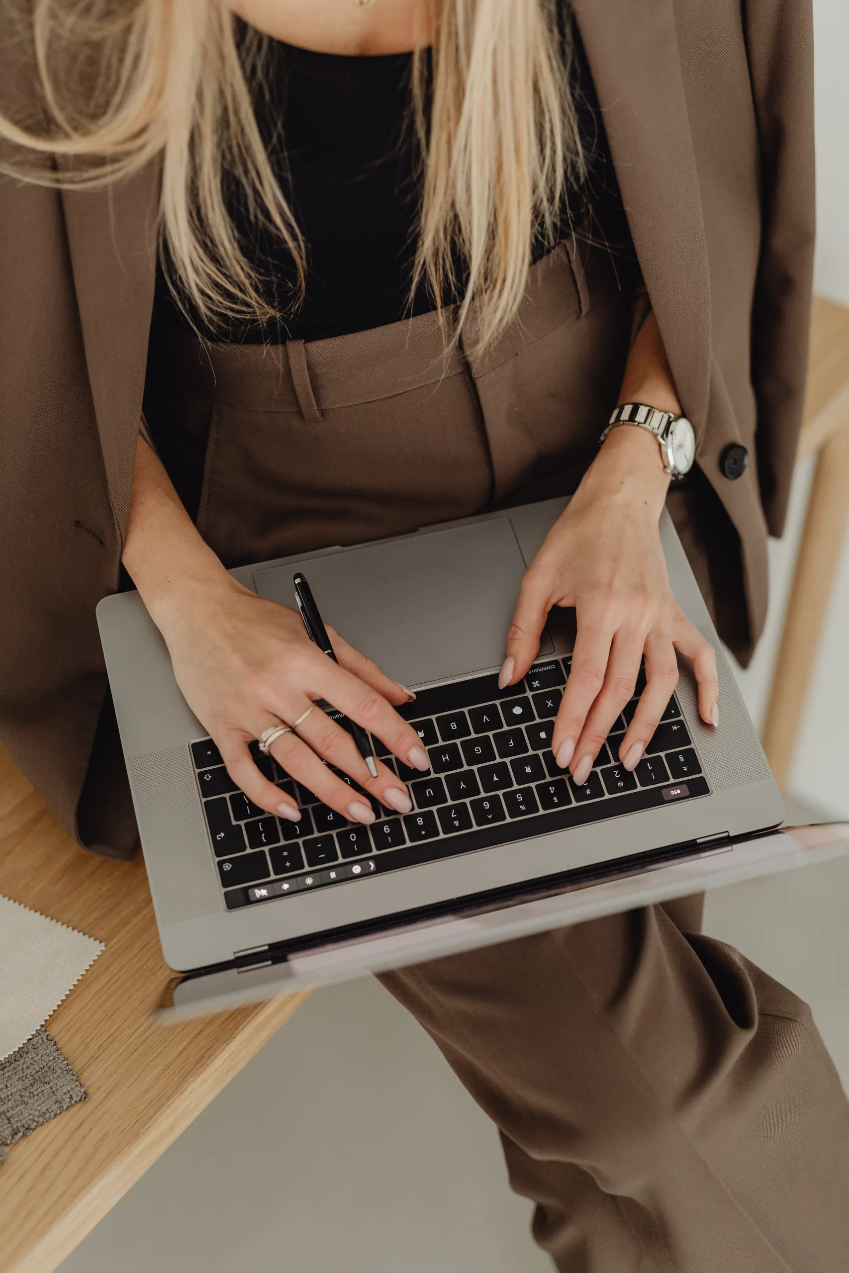 Blonde person in a brown blazer typing on a silver laptop at a desk.