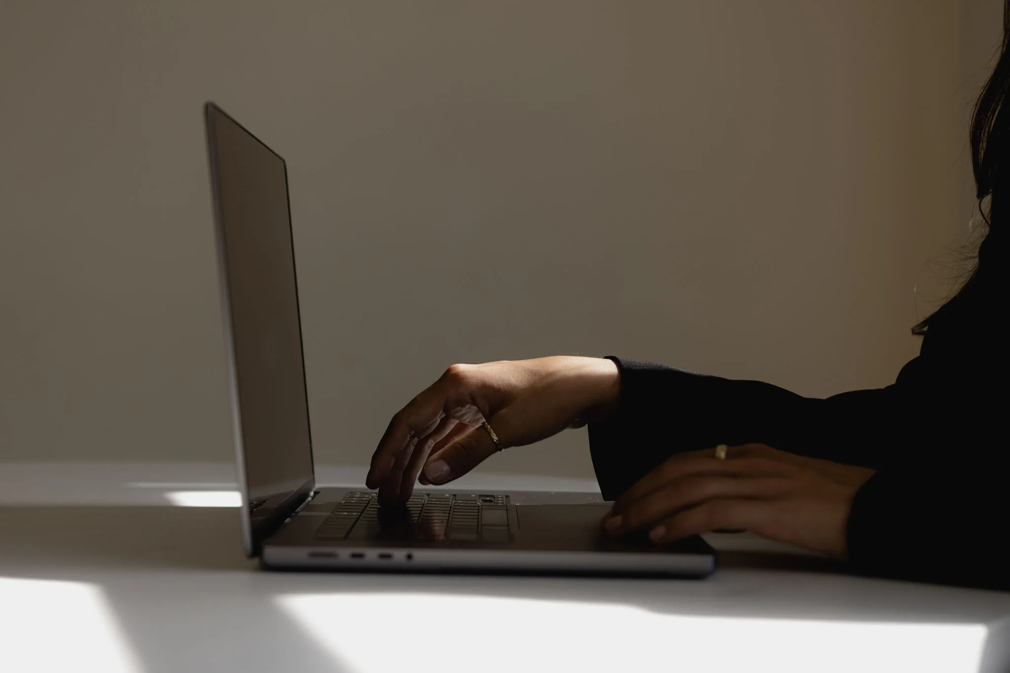 Hands typing on a laptop at a white desk in soft light. — website tips for wedding photographers