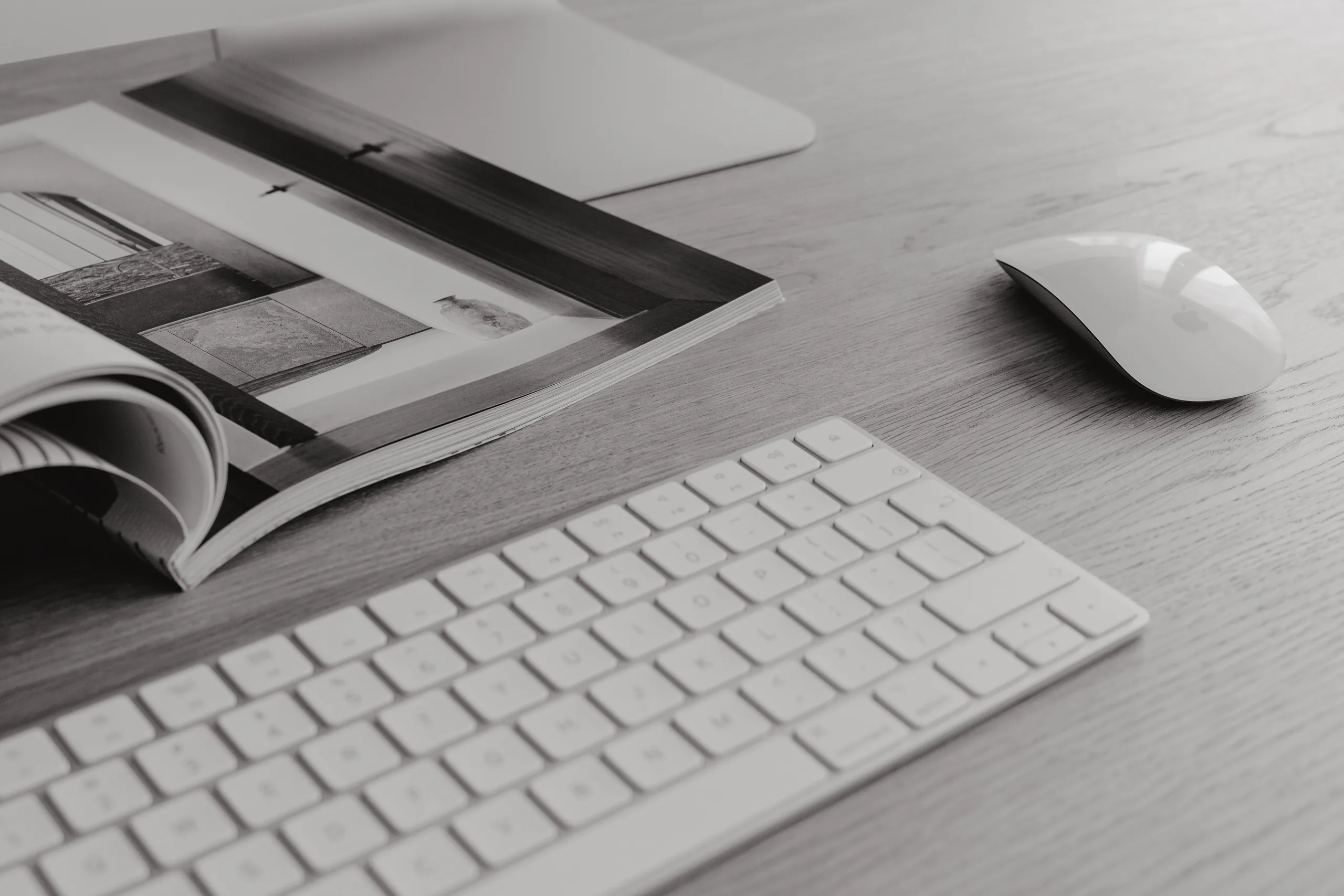 Keyboard, mouse, and open magazine on a clean wooden desk.