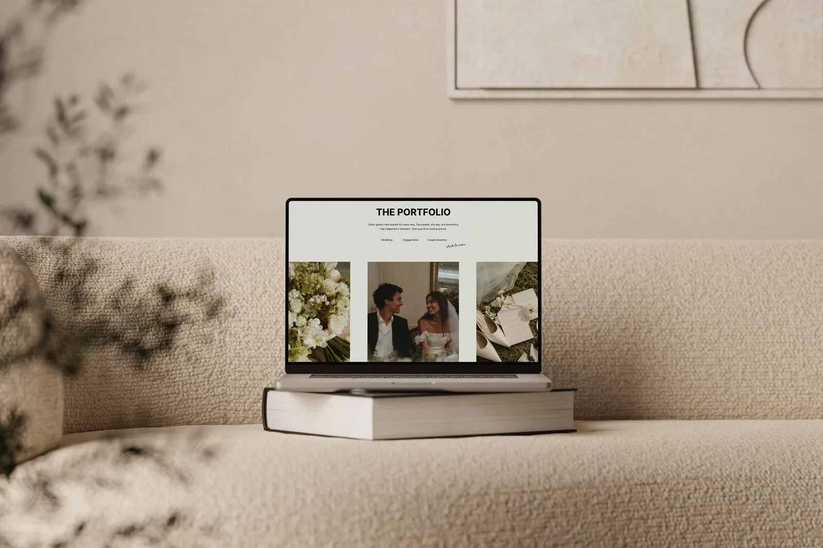 Laptop on stacked books displaying a portfolio website on a beige couch.