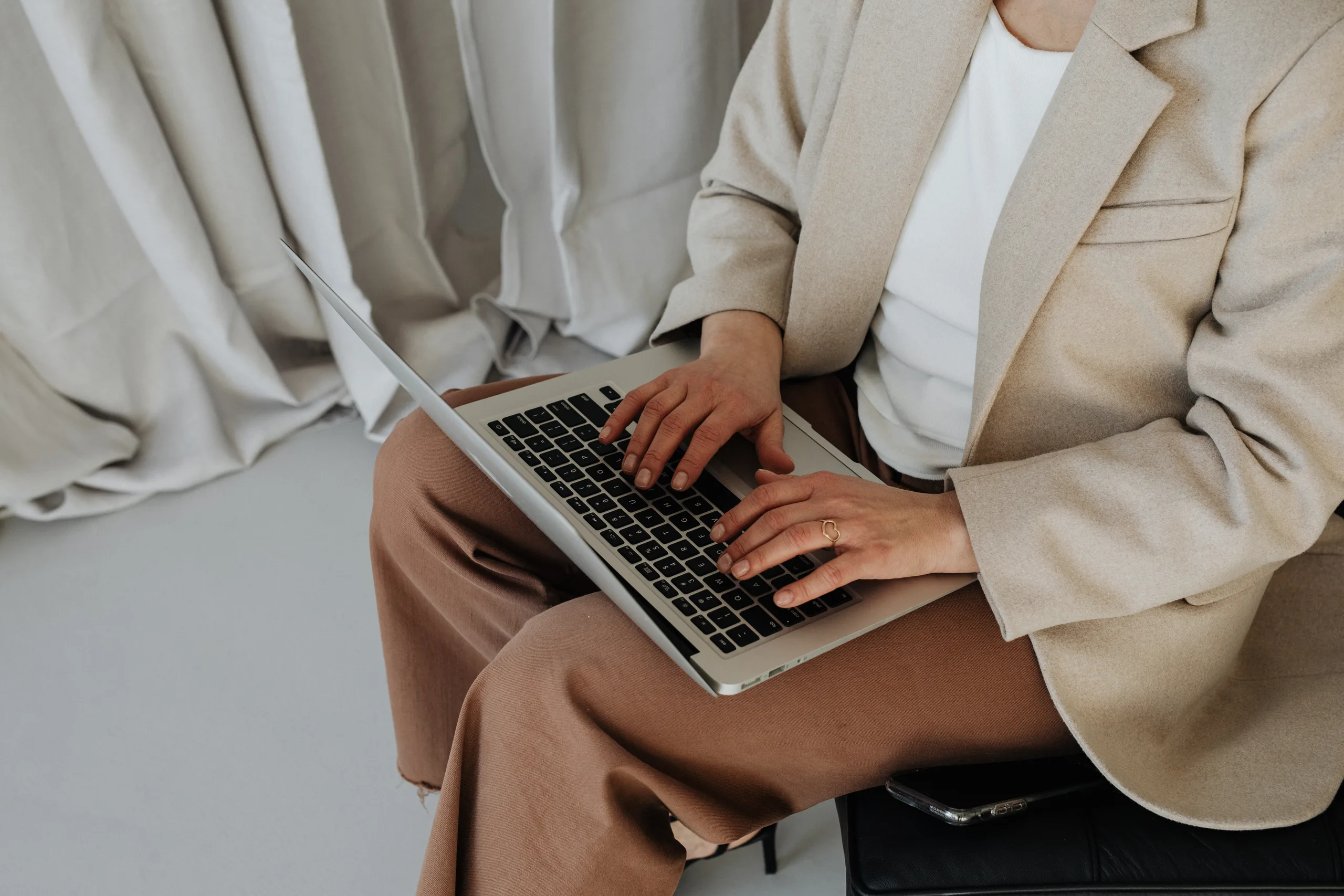 Person in a beige blazer typing on a laptop against a neutral backdrop.