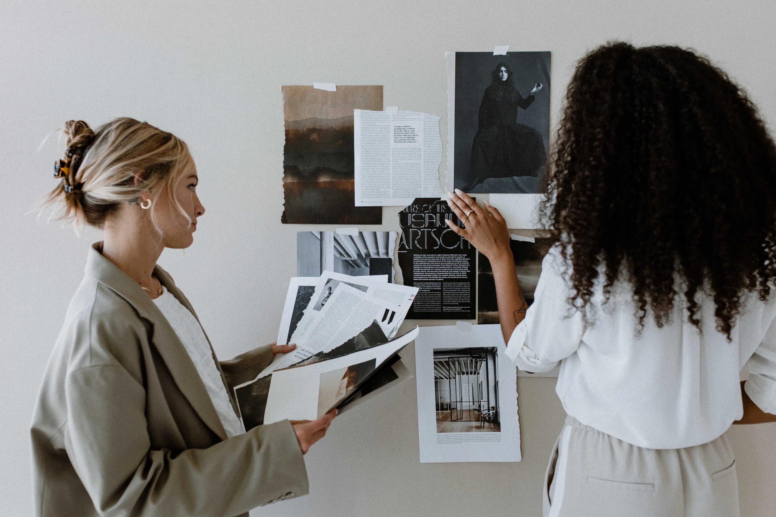 Two women arranging printed pages on a wall mood board. — showit templates for photographers