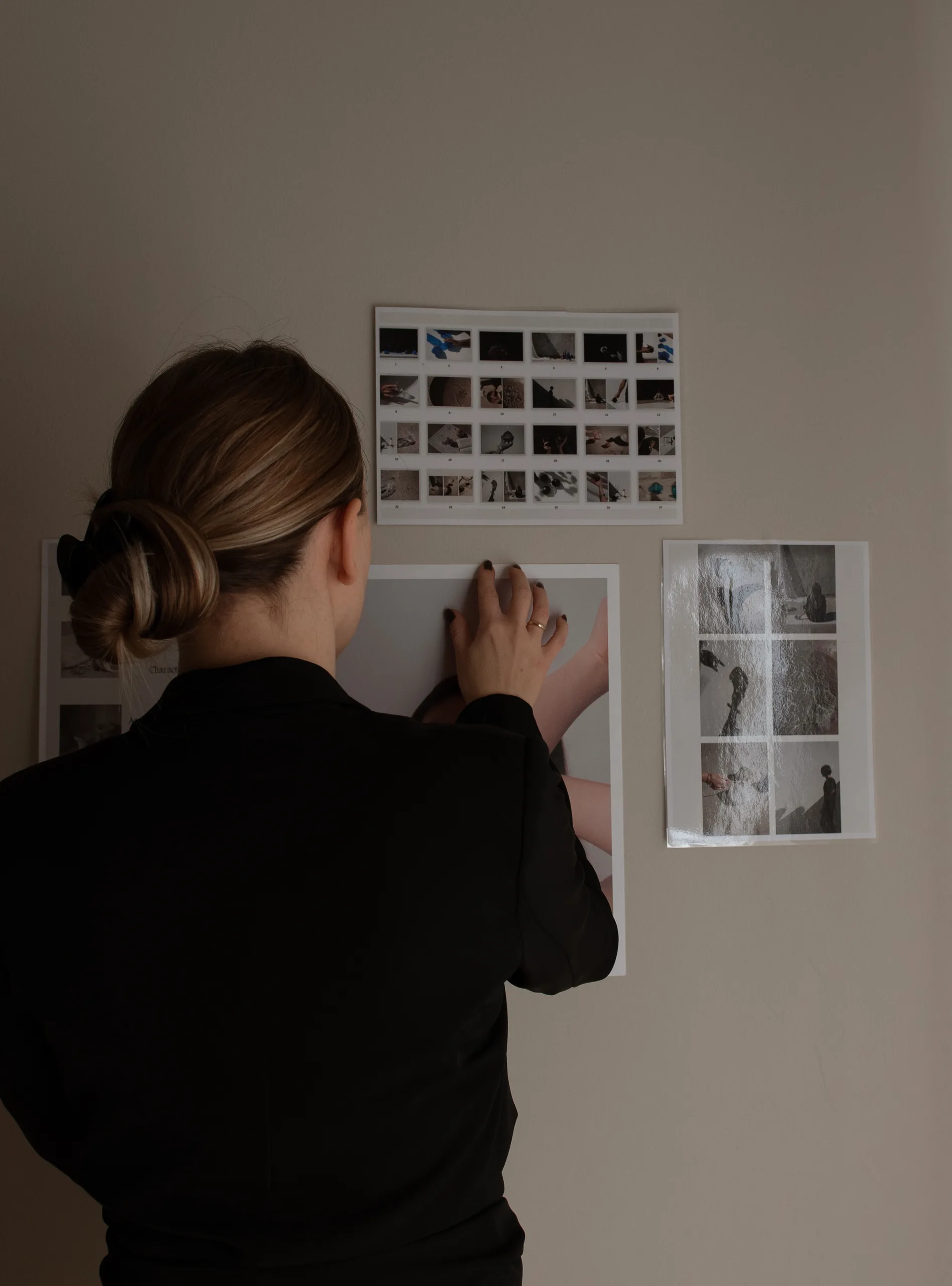 Person pinning printed images on a wall in a softly lit room.